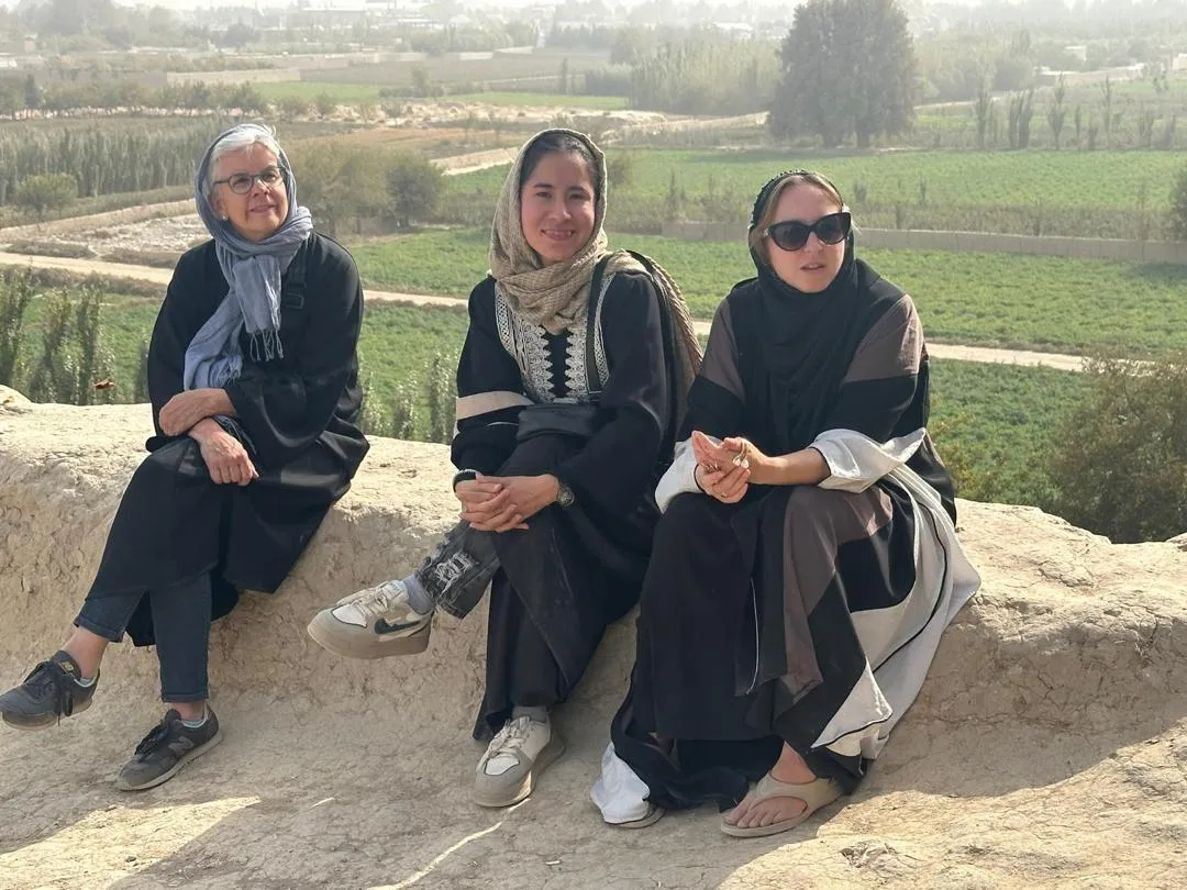 Female travelers sitting beside their female tour guide on the ancient walls of Balkh.